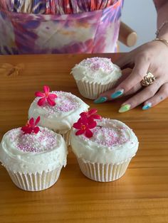 three cupcakes with white frosting and pink flowers on them sitting on a table