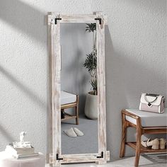 a large white wooden mirror sitting on top of a floor next to a chair and potted plant