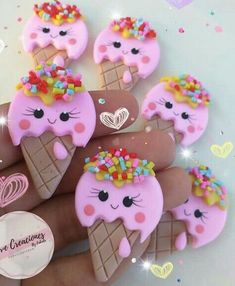 pink ice cream cones with sprinkles and hearts on their faces are being held by someone's hand