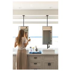 a woman standing in front of a kitchen sink holding a wine glass and looking out the window