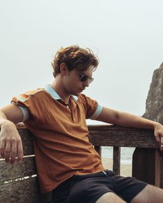 a man sitting on top of a wooden bench next to the ocean with his hands on his knees