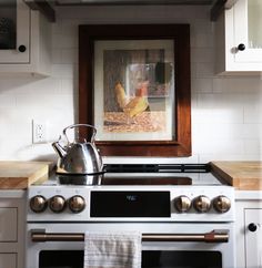 a white stove top oven sitting inside of a kitchen next to a painting on the wall