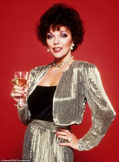 a woman holding a glass of wine in her right hand and wearing a gold jacket