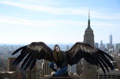 a woman sitting on top of a tall building with wings spread out over her body