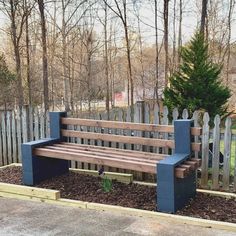 a wooden park bench sitting in the middle of a flower bed next to a fence