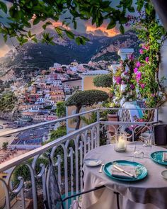 an outdoor table with plates and glasses on it overlooking the ocean, town and mountains in the distance