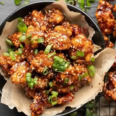 chicken wings with sesame seeds and green onions in a black bowl on top of a table