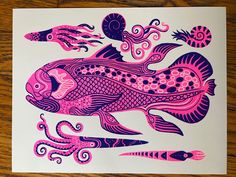 a pink and purple fish with an octopus on it's back is sitting on a wooden surface