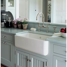 a white kitchen sink sitting under a window next to a counter top with bowls of fruit on it