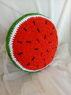 a knitted watermelon cushion sitting on top of a white cloth covered sheet