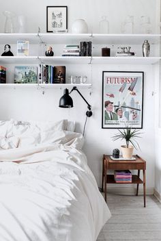 a bed with white sheets and pillows in a bedroom next to a shelf filled with books