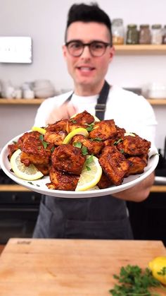 a man holding a plate with chicken wings and lemons