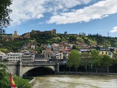 a bridge over a river in front of a city with buildings on the hill behind it