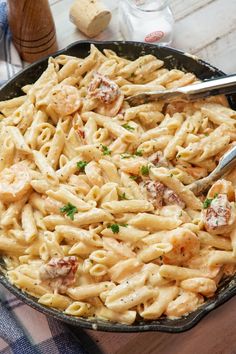 a skillet filled with pasta and meat on top of a wooden table