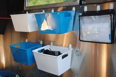 three bins are hanging on the side of a metal wall with two blue and one white containers