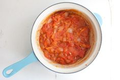 a pot filled with tomato sauce sitting on top of a table next to a blue spoon