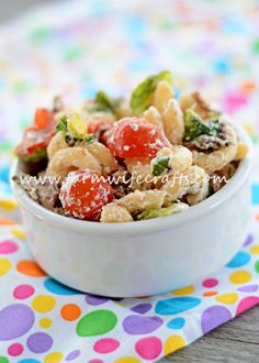 a white bowl filled with pasta salad on top of a polka dot table cloth next to a colorful napkin