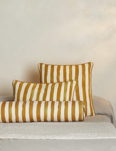 two yellow and white striped pillows sitting on top of a bed next to each other