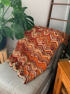 a crocheted blanket sitting on top of a couch next to a potted plant