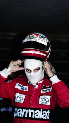 a man wearing a white mask and red racing suit is covering his face with one hand