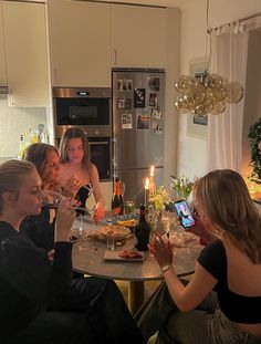 four women sitting at a table with food and drinks in front of them while one woman takes a photo on her phone