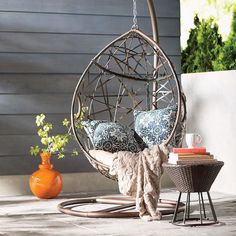 a hanging chair with pillows on top of it next to a table and potted plant