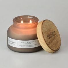 a candle that is sitting next to a wooden lid on a white surface with the words, soft canniere amber