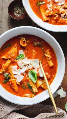 two bowls filled with pasta and sauce on top of a wooden table