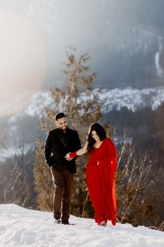 a man and woman holding hands while standing in the snow on top of a mountain