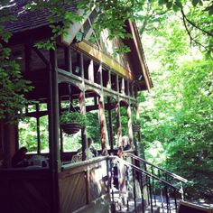 a wooden house in the woods with lots of trees around it and people standing on the porch