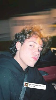 a young man with curly hair wearing a black shirt and neck tie, sitting in a car