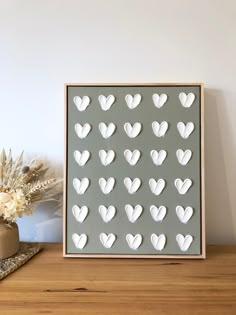 a wooden frame with white hearts cut out of it on a table next to a potted plant