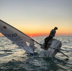 a man riding on the back of a sailboat in the ocean at sunset or dawn