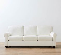 a white couch sitting on top of a hard wood floor next to a white wall