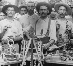 a group of men standing next to each other in front of a table full of machines