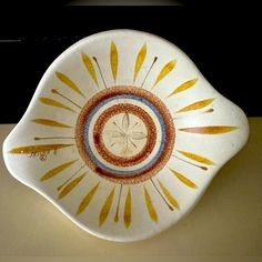 a white bowl with yellow, blue and red designs in the center on a table