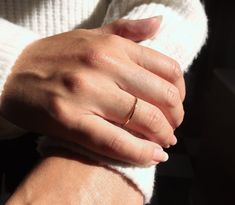 a woman's hand with a gold ring on her left and a white sweater