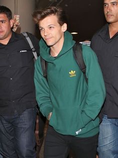 a man in a green hoodie is walking through an airport with other men behind him