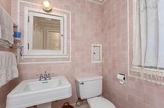 a white toilet sitting next to a sink in a bathroom under a window with curtains