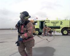 two fire fighters are standing in front of a green truck with hoses attached to it