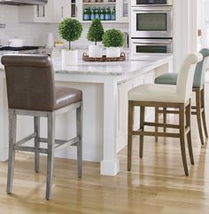 a kitchen with white cabinets and countertops has two stools at the center of the island