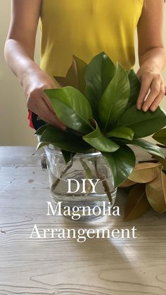 a woman is arranging flowers in a vase on a table with the words diy magnolia arrangement