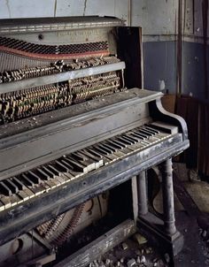 an old piano sitting in the corner of a room with peeling paint and broken windows