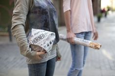 two people standing next to each other on a sidewalk with bread wrapped in newspaper paper