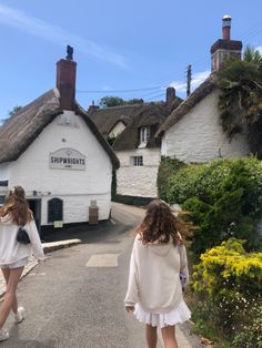 two girls walking down the road in front of some white buildings with thatched roofs