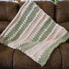 a crocheted blanket sitting on top of a brown couch next to a plant