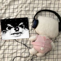 a teddy bear with headphones on laying next to a painting and ear phones in front of it