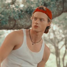 a young man wearing a red bandana standing in front of trees