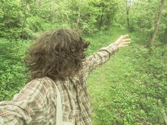 a person standing in the woods with their arms spread out and looking at the trees