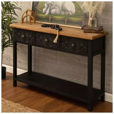 a console table with two drawers and a painting on the wall behind it, next to a potted plant